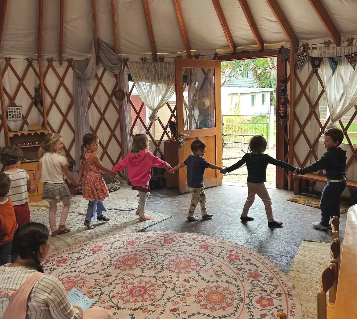 A group of children hold hands and form a circle inside a round structure.