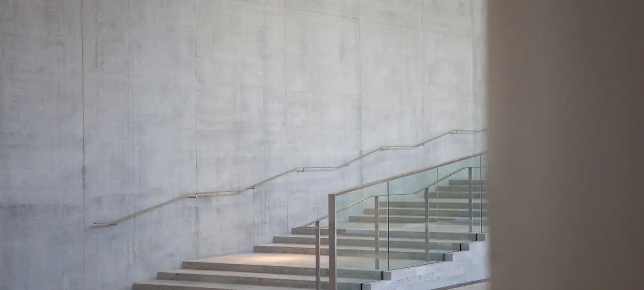 A modern staircase features glass railings and a smooth concrete wall.