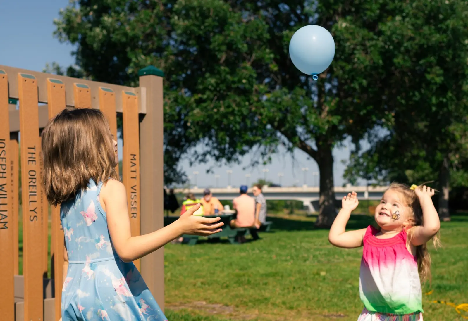 Two children play with a light blue balloon in a park.