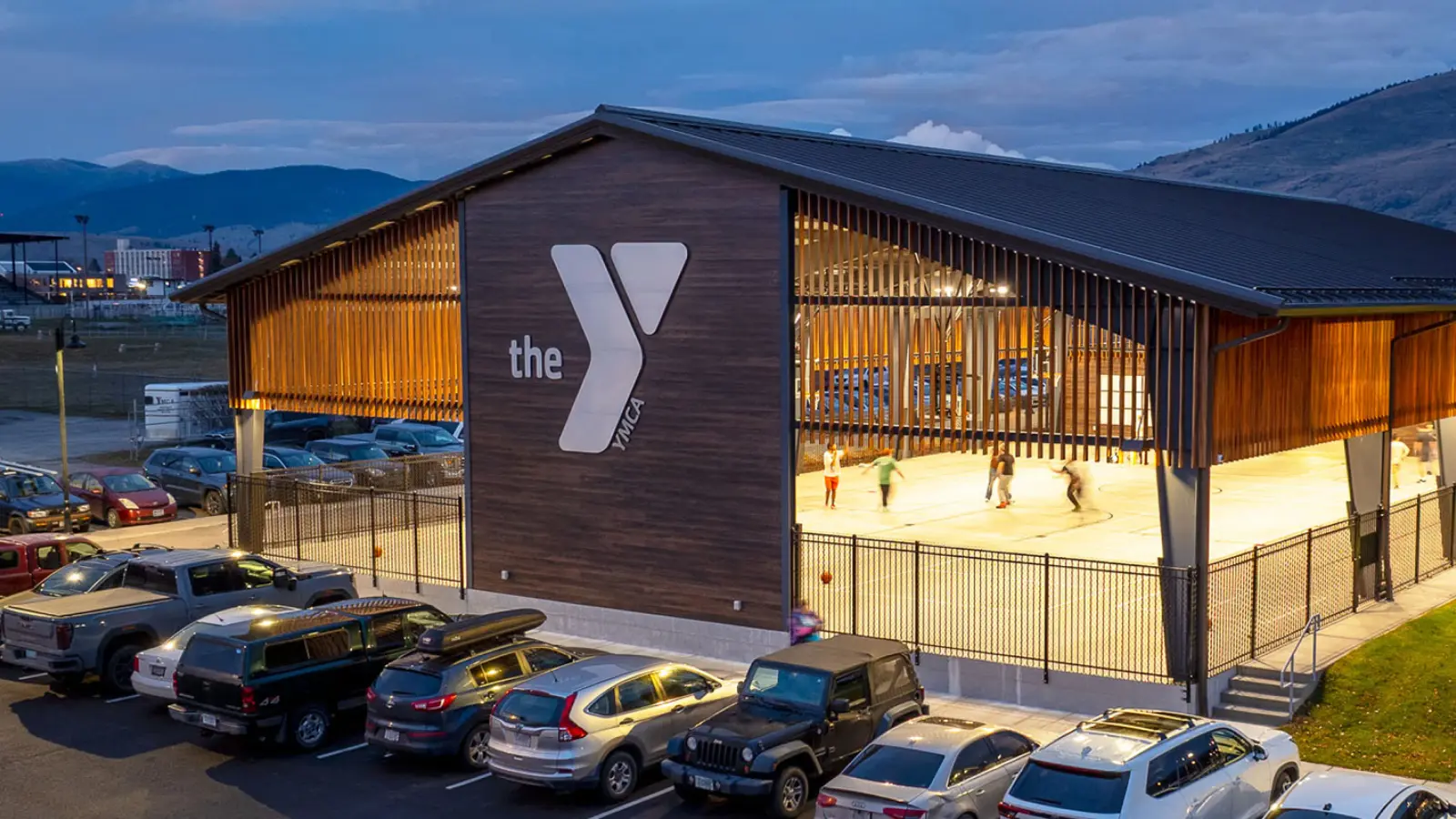 an aerial view of the missoula ymca's covered outdoor basketball court. a group of people play basketball in the open-air structure