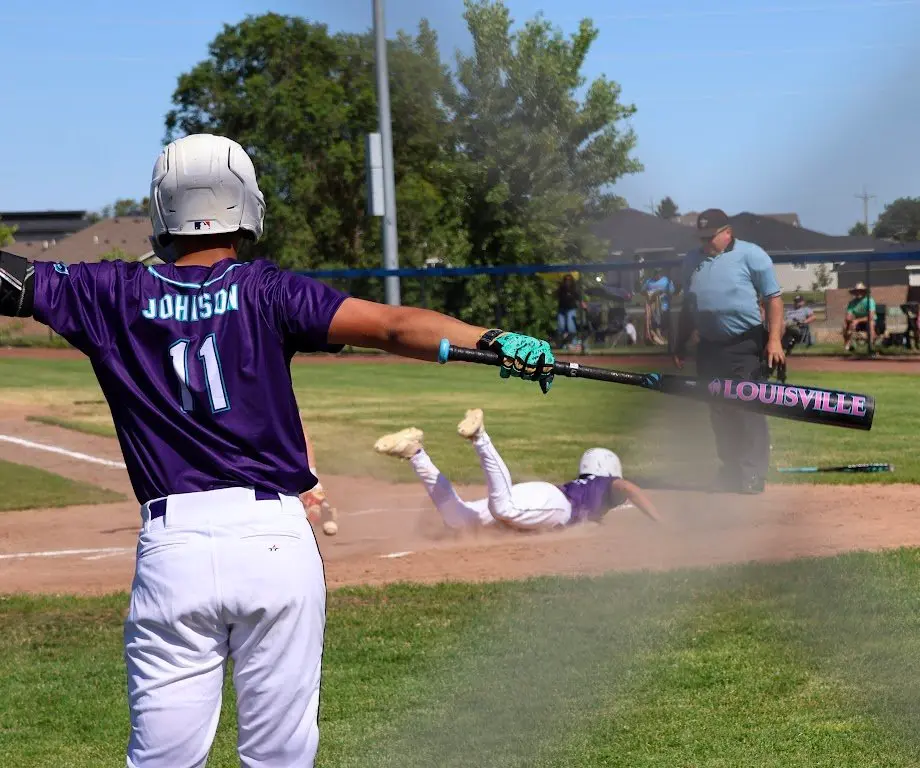 A baseball player watches a teammate slide into base during a game.