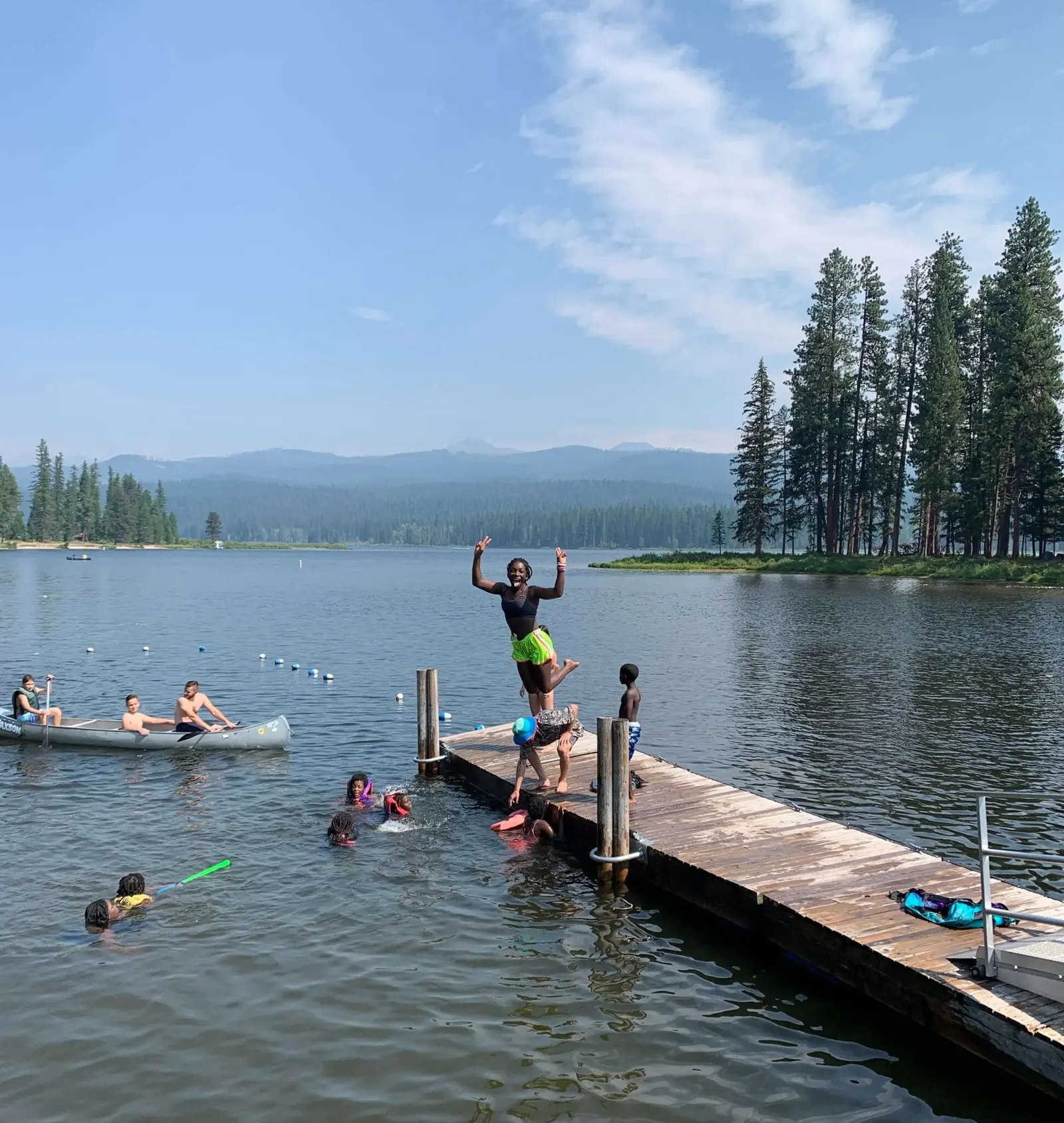 A group of children are active at a lake with some swimming and others jumping off a dock.