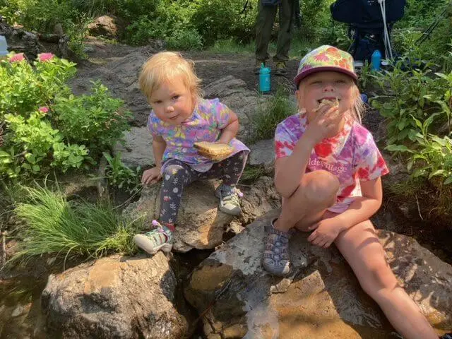 Two children sit on rocks in a natural outdoor setting.