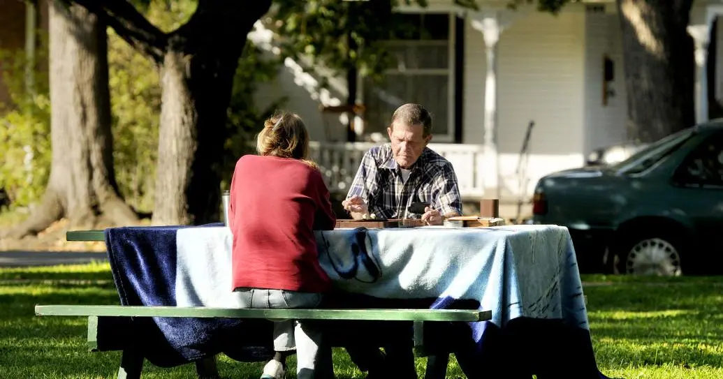 An older couple sits at an outdoor picnic table playing a game.