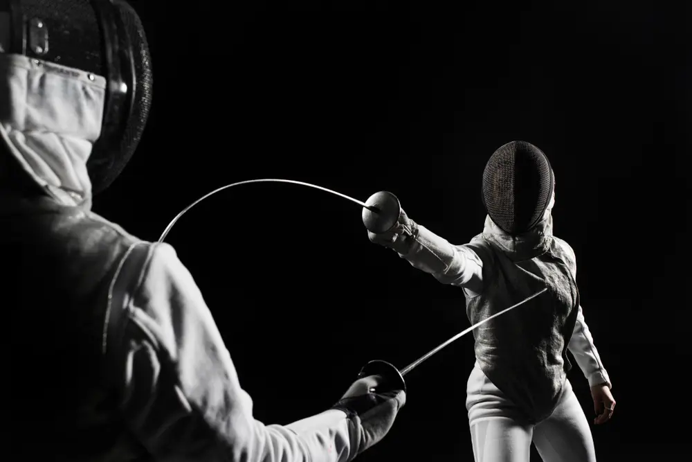Two fencers wearing protective gear and masks are engaged in a match against a black background.