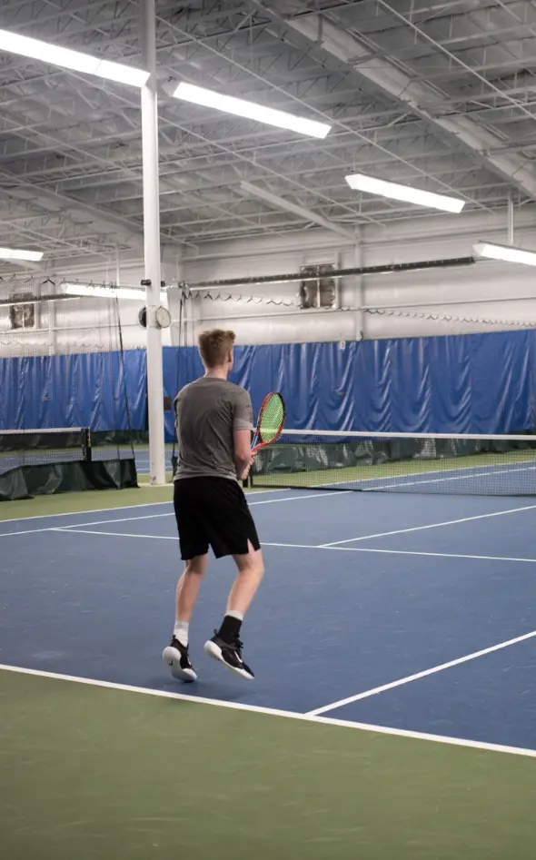 A young man leaps while playing tennis on an indoor court.