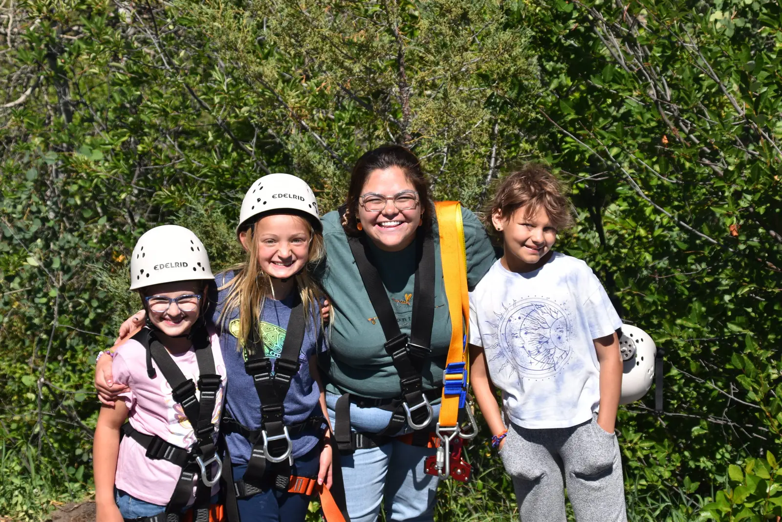 An instructor and three children wearing helmets and harnesses pose together outdoors.