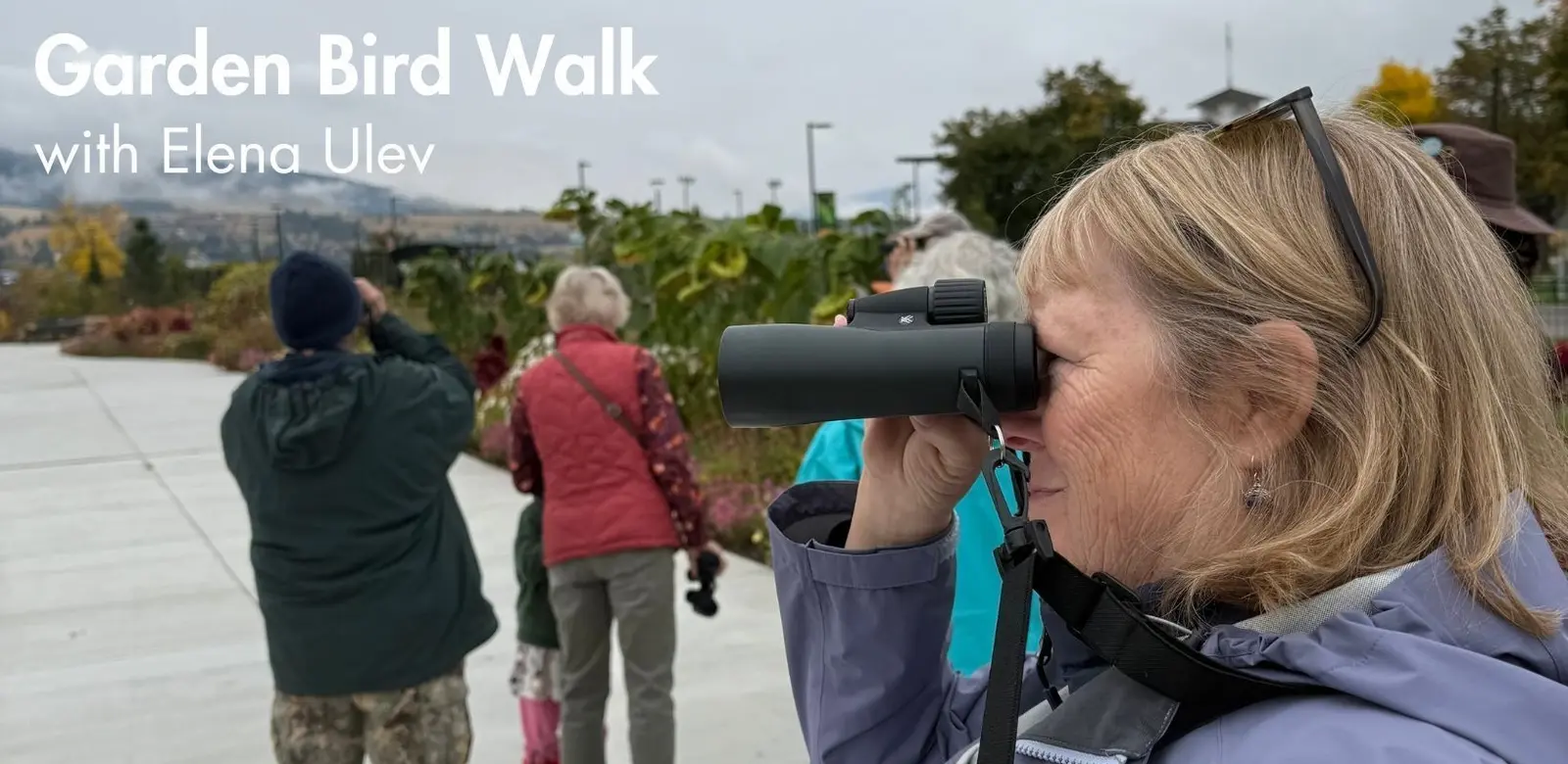 A woman looks through binoculars in a garden with others nearby.