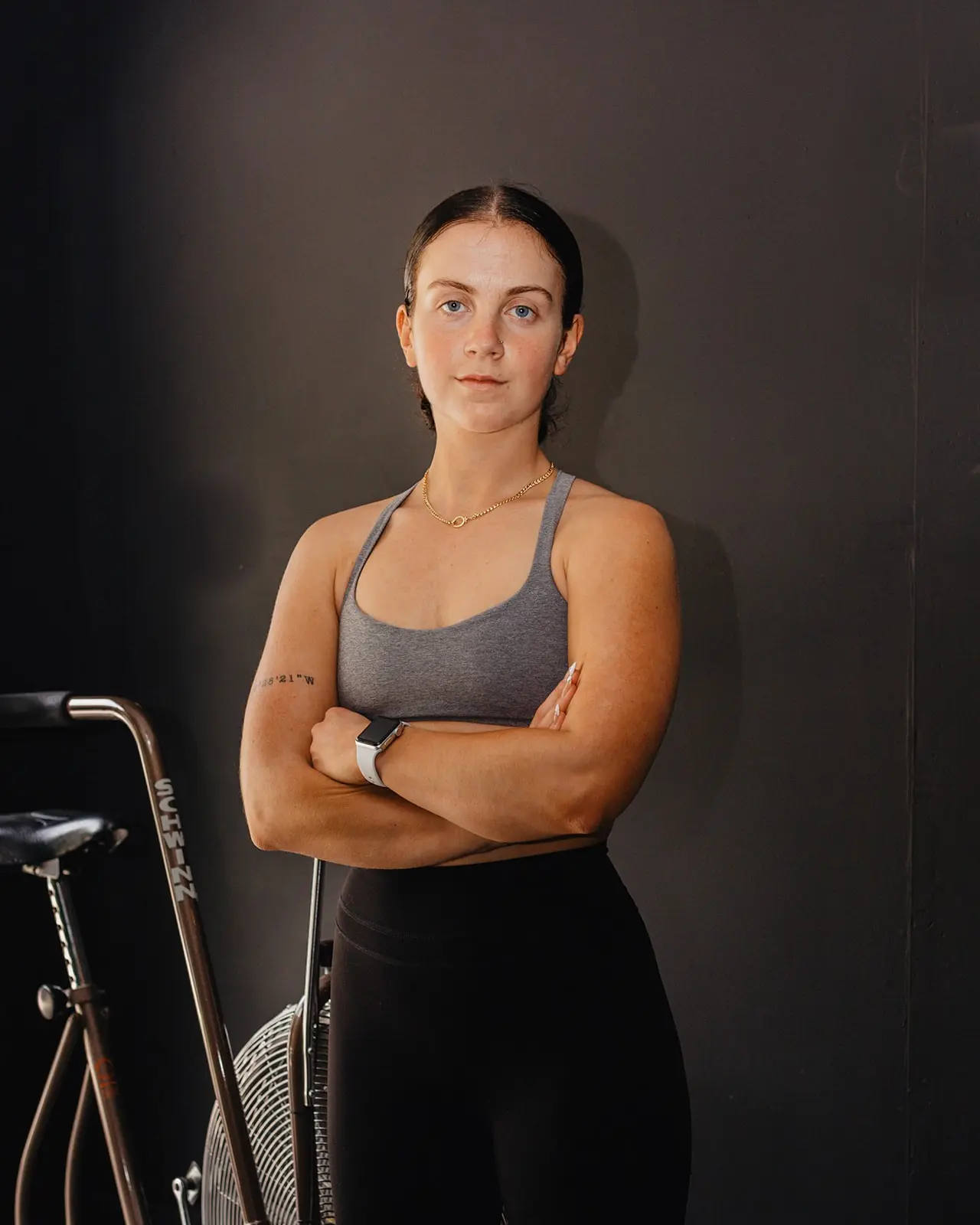 A woman stands with her arms crossed in front of a stationary bike.