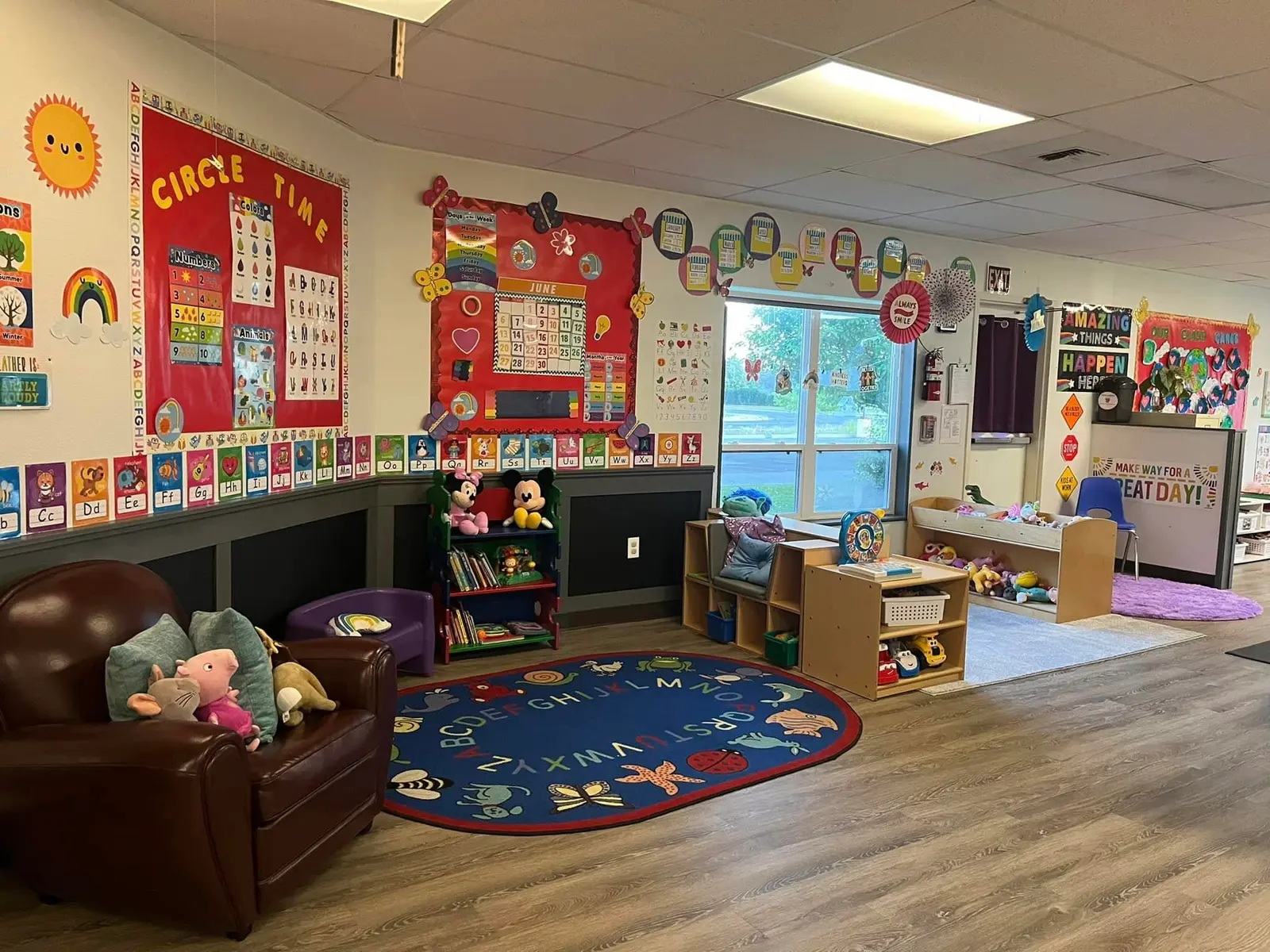 A brightly decorated preschool classroom features child-sized furniture and educational displays on the walls.