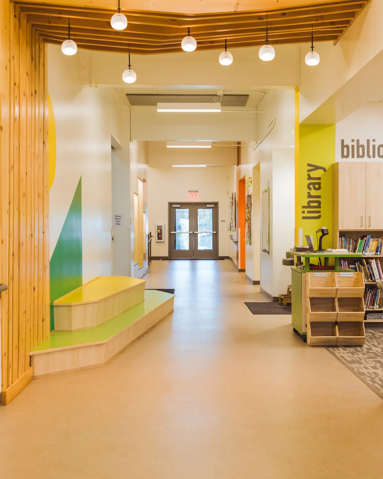 A brightly lit interior hallway features wooden accents, a colorful mural, and a library section.