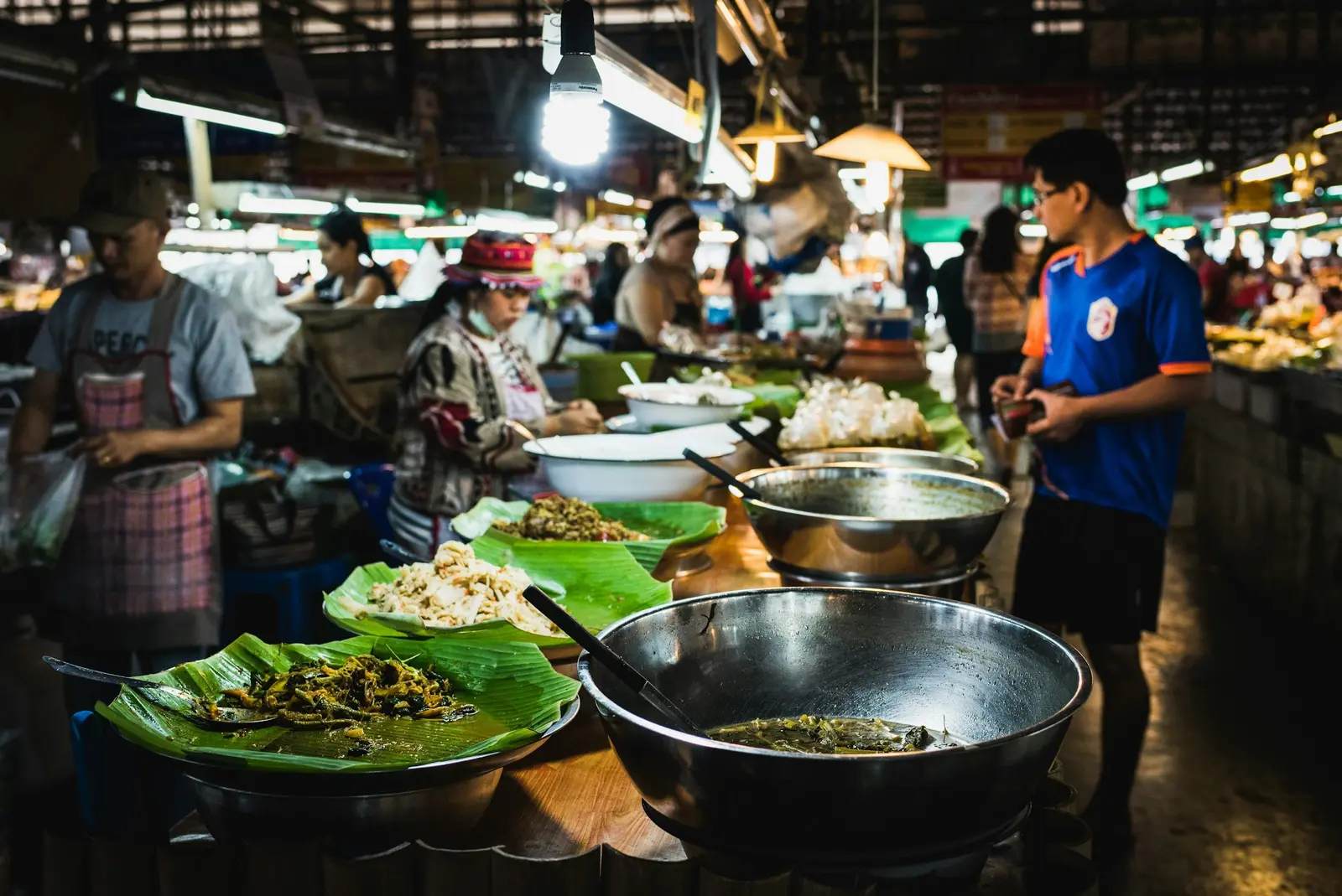 A food market stall displays several bowls of prepared dishes on banana leaves.
