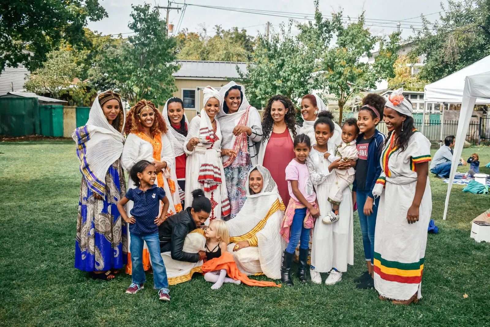 A group of women and children are posing together outdoors in an grassy area.