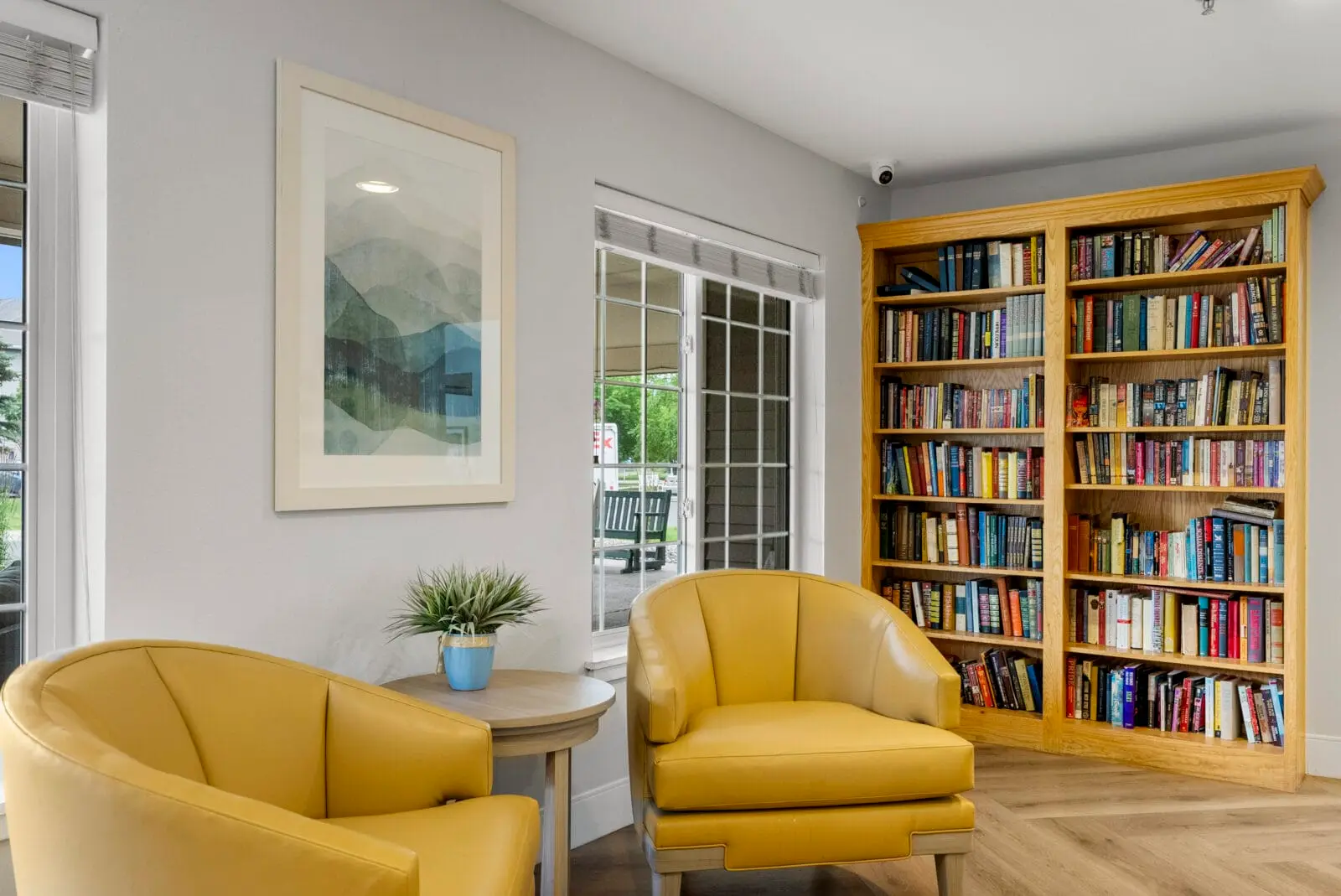 Two yellow armchairs sit in a room beside a bookshelf and a small table.