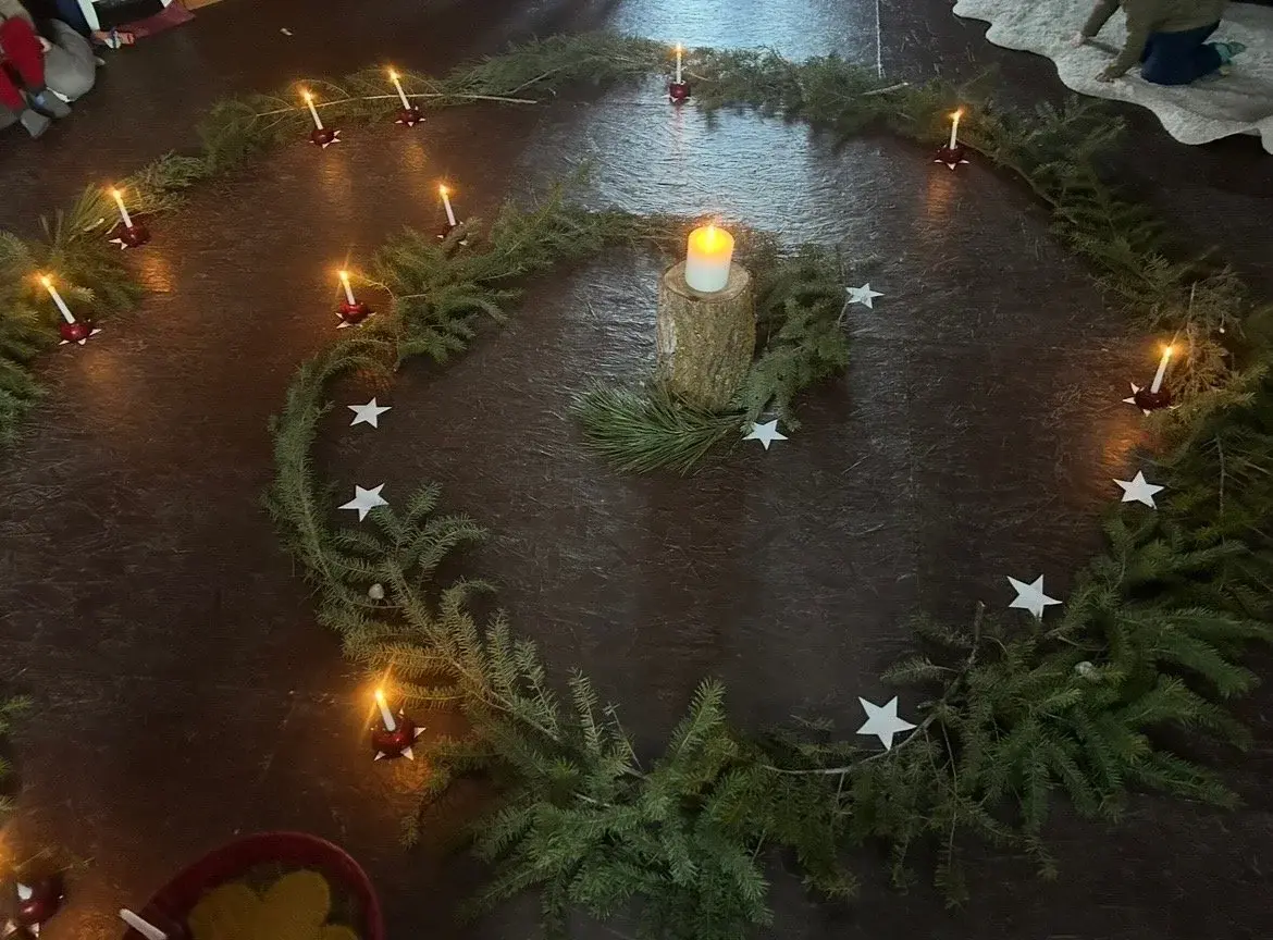 A spiral of evergreen branches and candles is arranged on the floor with white paper stars.