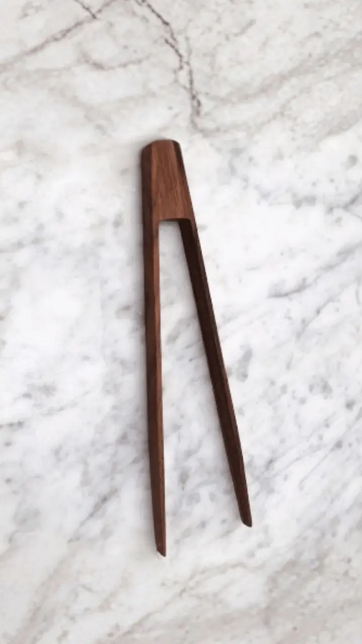 A pair of wooden kitchen tongs rests on a marble surface.