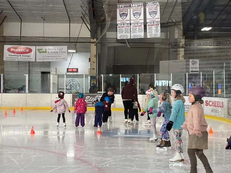 A group of children participate in an ice skating lesson at an indoor rink.