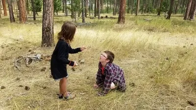 A girl and a boy are exploring in a wooded area.