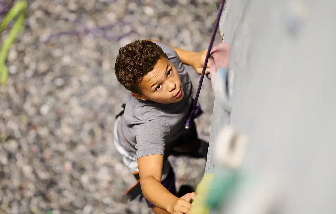 A child reaches for a hold while climbing a rock wall.