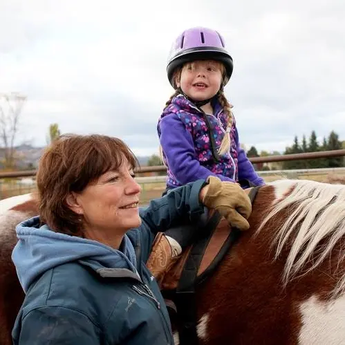 A child sits on a horse while an adult instructor guides them.