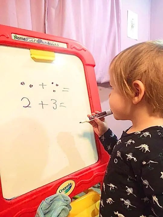 A child is drawing math equations on a small whiteboard.