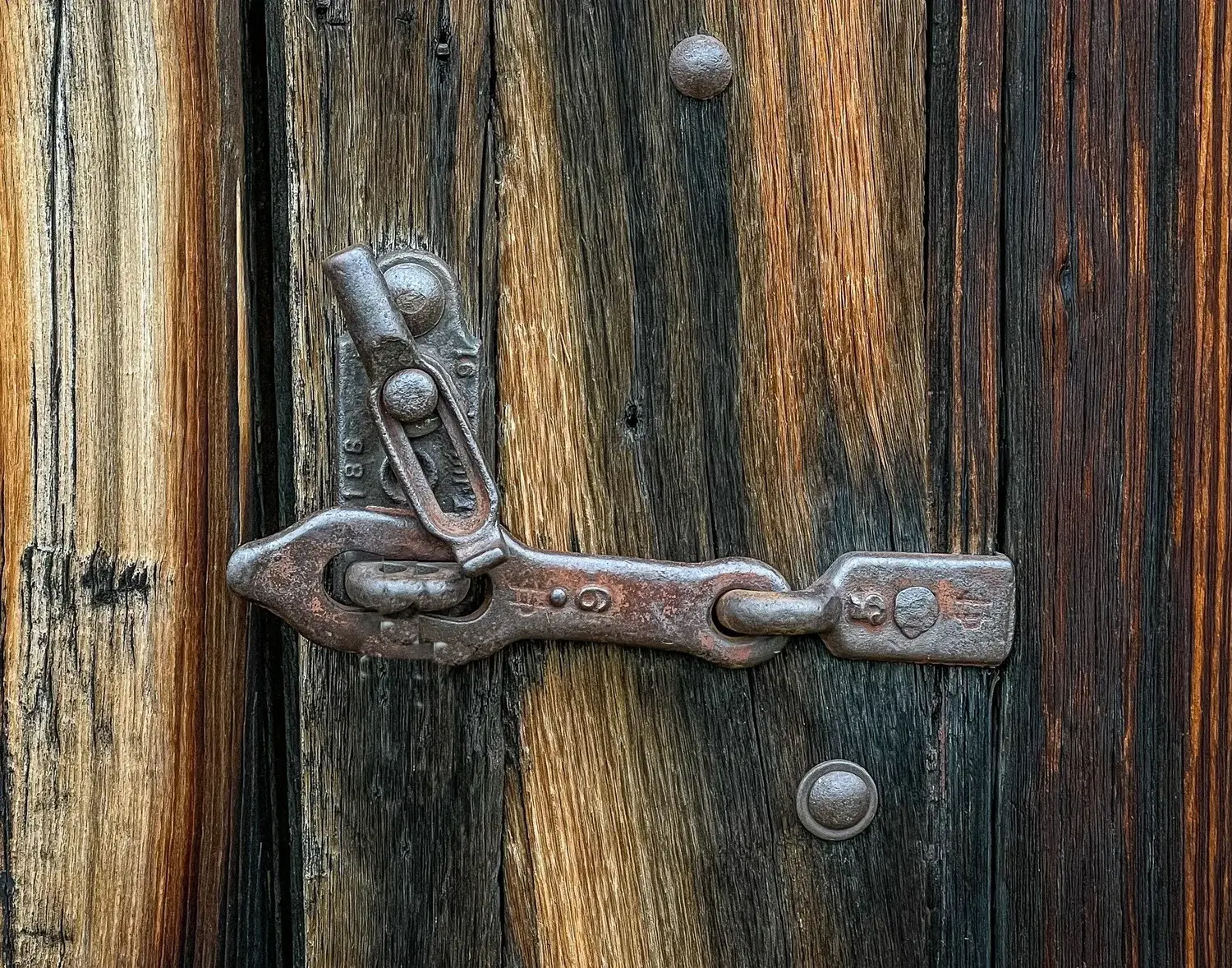 An old, rusty metal latch is secured on a weathered wooden door.