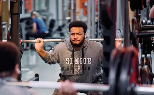 A man performs a barbell squat in a gym.