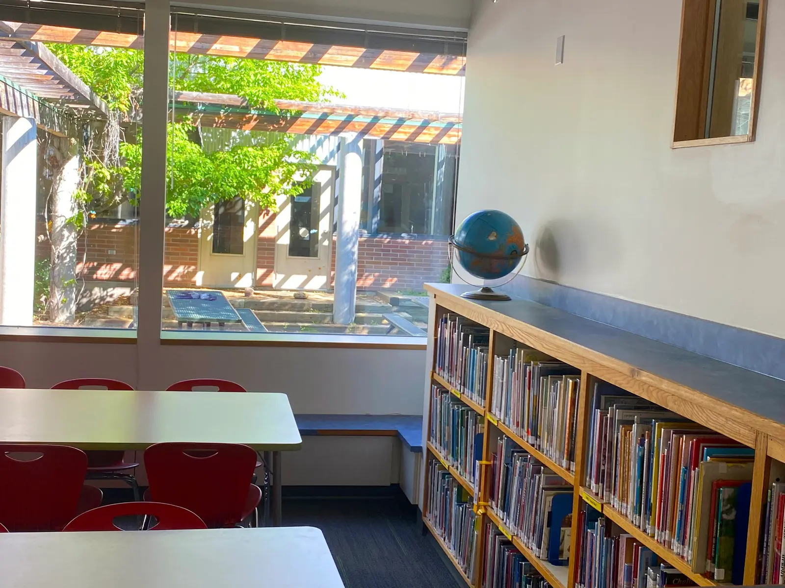 A bright library room features tables, red chairs, and a bookshelf topped with a globe.
