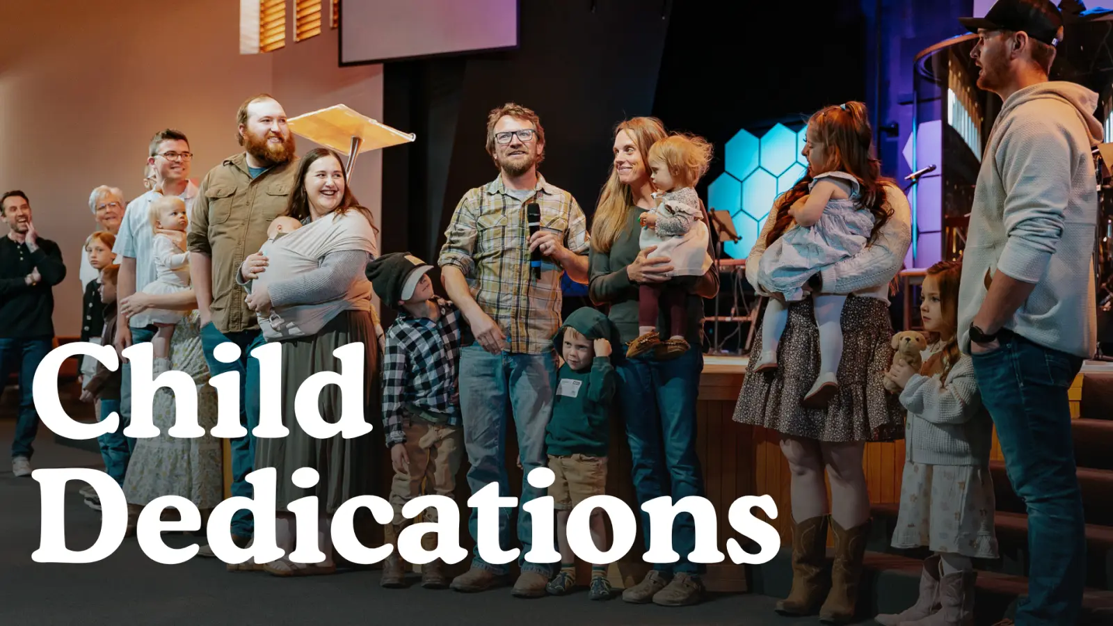 Several families stand on stage together during a child dedication event.