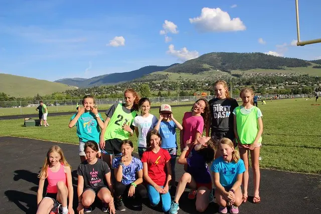 A group of girls posing for a photo on an outdoor track with mountains in the background.
