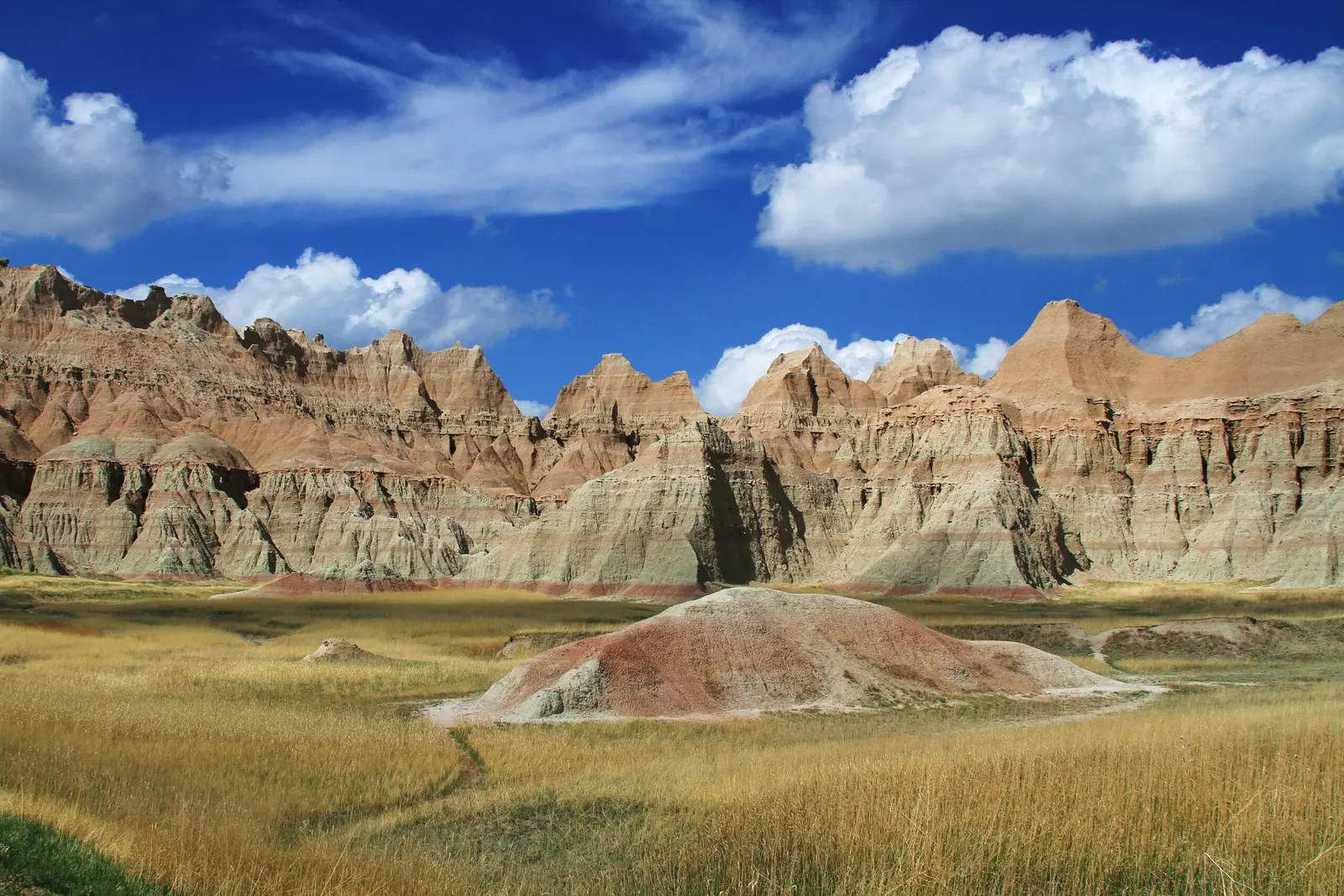 A scenic landscape featuring layered rock formations above a grassy field under a sunny sky.