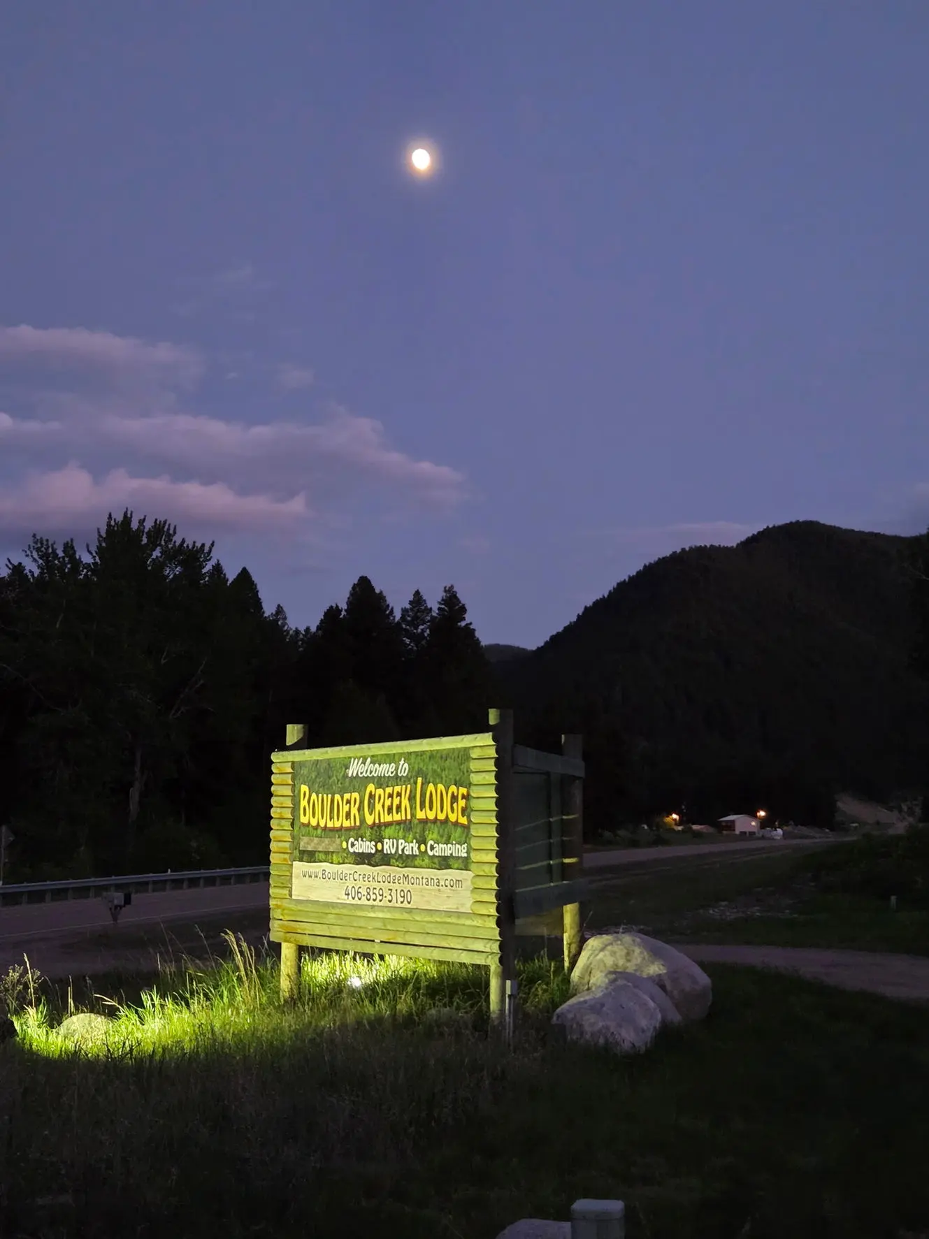 An illuminated lodge sign sits outside at dusk under the moon.