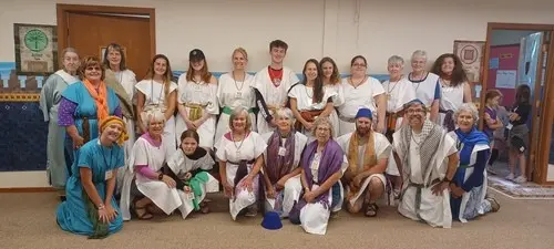 A large group of people dressed in historical-style costumes pose together indoors.